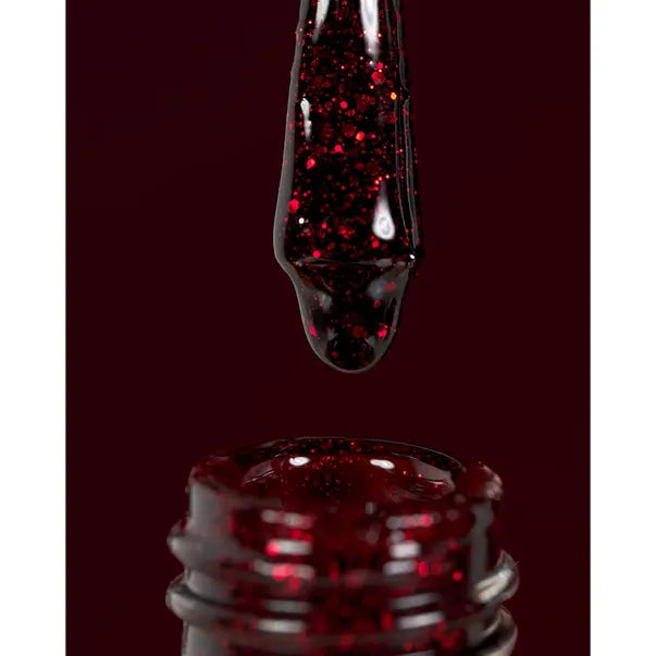 Red glittery liquid being dripped from a dropper into a container on a dark background.