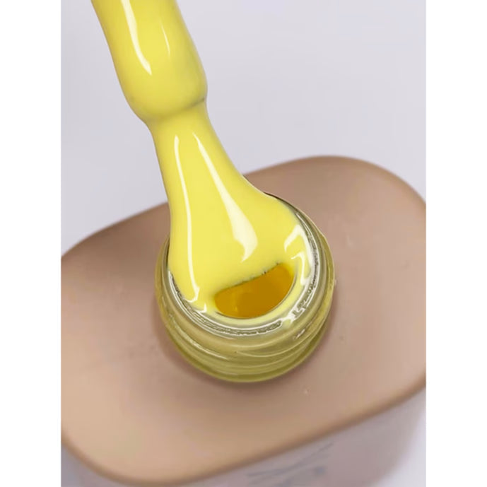 Yellow nail polish being applied to a nail with a white background