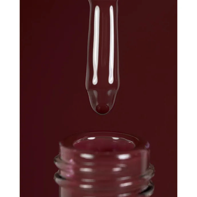 Close-up of a nail polish bottle with a droplet of dark red nail polish on a matching background
