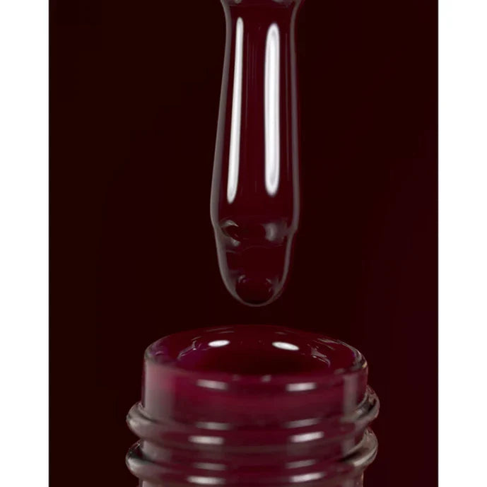 Close-up of a dark red nail polish bottle with a droplet of polish above it on a black background.