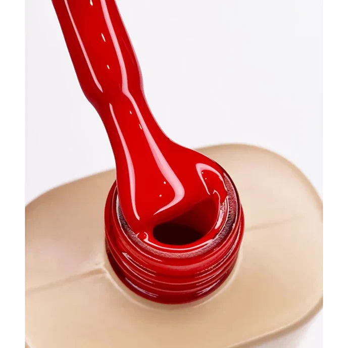 Red gel polish being poured into a beige container on a white background