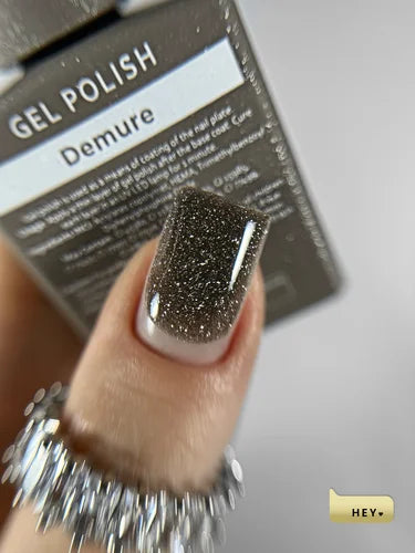 Nail with gel polish showing 'Demure' brand name, close-up on a neutral background.