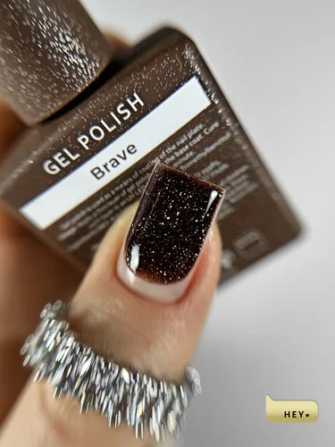 Gel polish with 'Brave' color on a finger, next to its packaging.