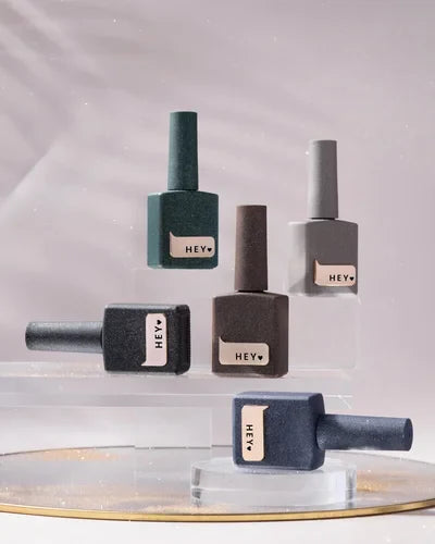 Set of nail polish bottles with 'HEY' label on a reflective surface