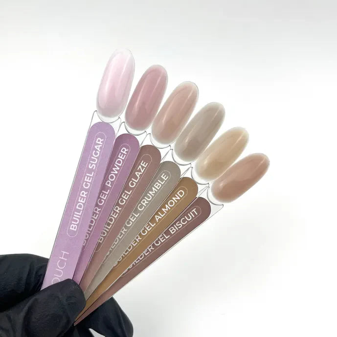 Set of TOUCH Builder Gel Powder samples in various shades held by a gloved hand on a white background.