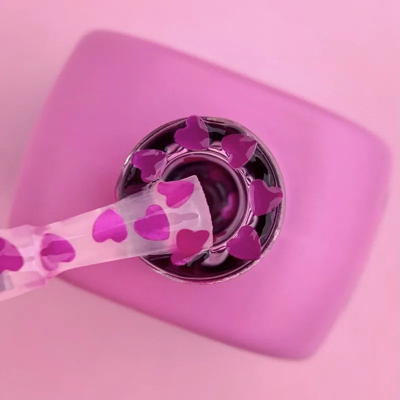 Pink spoon with heart patterns dipping into a pink container on a pink background